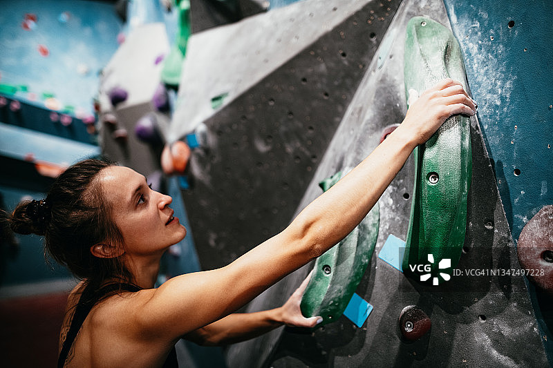 强壮的女人在大石墙上攀岩-室内攀岩图片素材