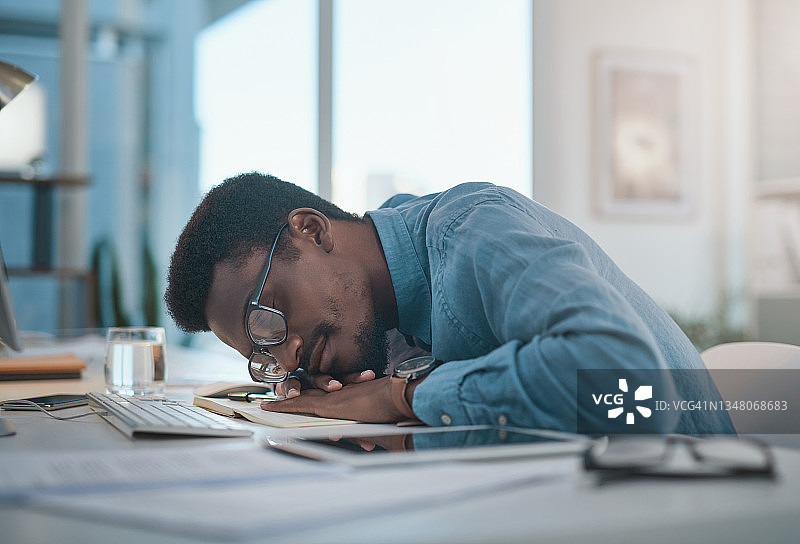一个年轻的商人在他的办公桌上睡觉在一个现代化的办公室图片素材