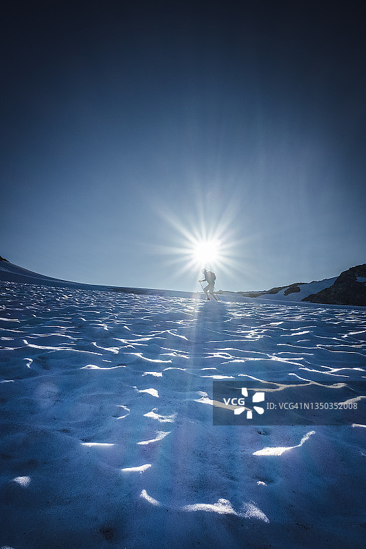 在太阳低垂的地平线上，徒步穿越冰雪覆盖的冰川图片素材
