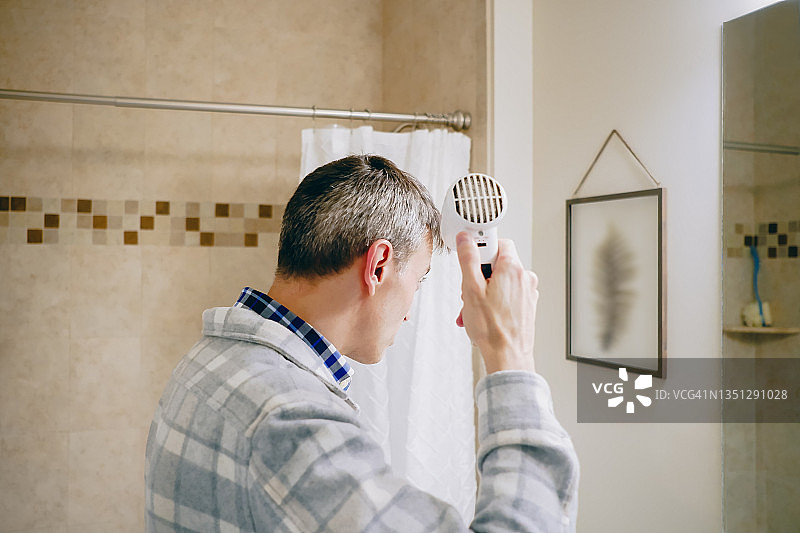 一名男子在浴室镜子前吹干头发图片素材