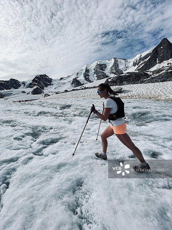 年轻女子拄着杆子和冰爪在冰川上奔跑图片素材