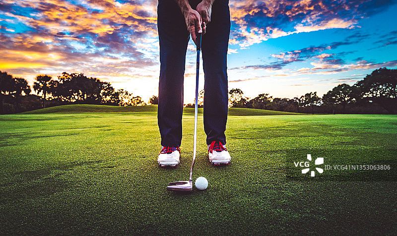 日落天空下的草地上的高尔夫球，穿着高尔夫鞋拿着球杆的无名高尔夫球手图片素材