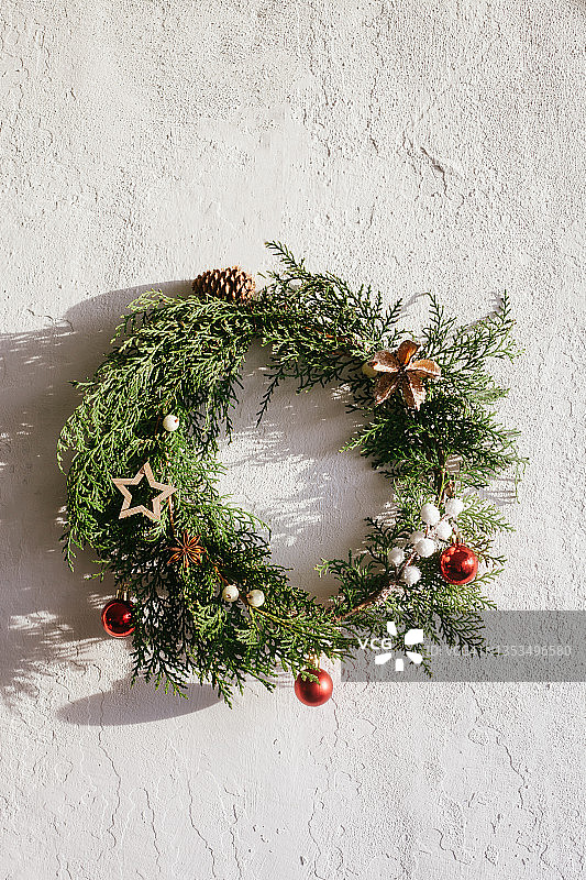 白色墙壁上用天然松枝、装饰品和浆果制成的常青圣诞花环。家居装饰DIY的想法。图片素材