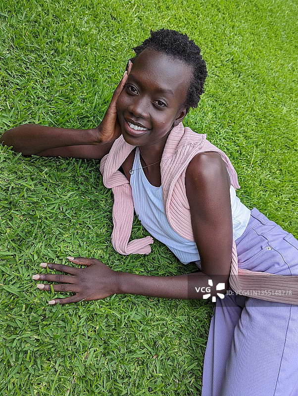 年轻女子躺在草地上微笑和摆姿势图片素材