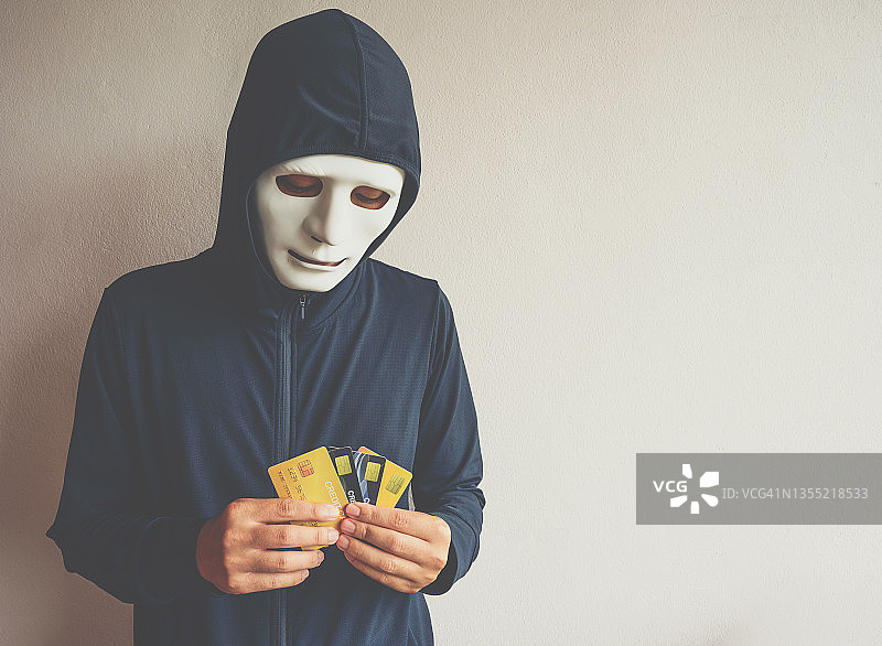 戴着黑客面具的神秘男子手里拿着一堆信用卡。图片素材
