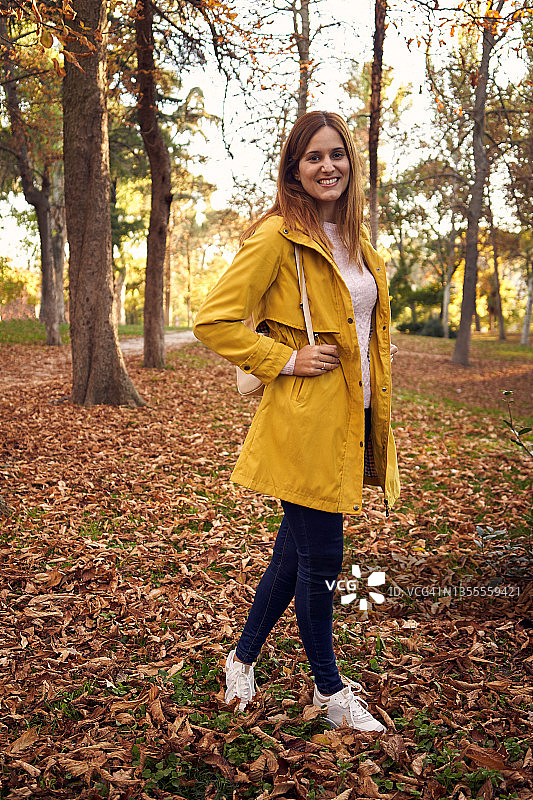 穿着便服和黄色外套的年轻女子在树木环绕的公园里。图片素材