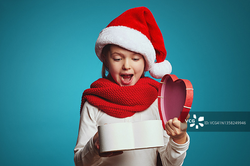震惊可爱的小女孩戴着圣诞帽拿着打开的礼物盒图片素材
