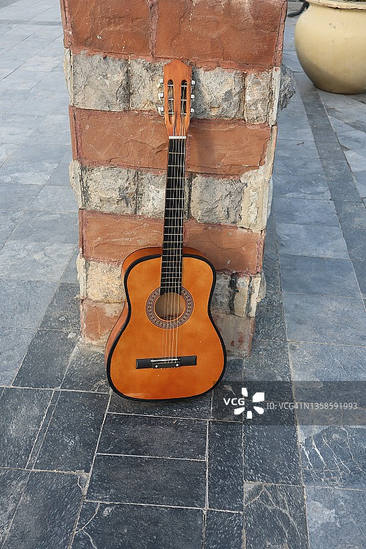 古典棕色吉他放置在棕色砖前-古典吉他对着砖墙和地板背景垂直方向图片素材