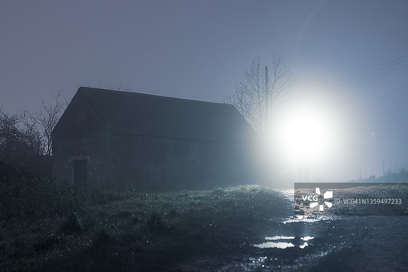 在一个雾蒙蒙的冬夜，一个废弃的谷仓背被点亮在乡间。图片素材
