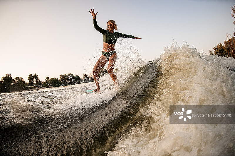 欢快的年轻女子骑在溅起水花的河水上冲浪。活跃的水上运动图片素材