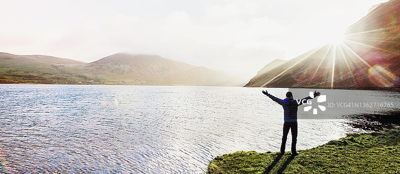 在阳光明媚的遥远湖畔，一个兴高采烈的人伸开双臂站在那里图片素材