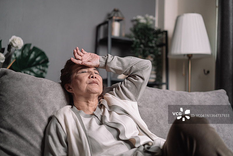一位老太太坐在家里的沙发上，对自己的生活忧心忡忡。老年女性生病或头痛。图片素材