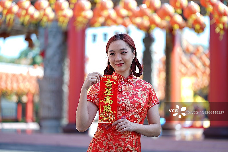 美丽的亚洲女人在中国新年穿旗袍拿红包，外语翻译为大运大利图片素材
