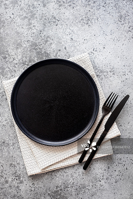 空黑色陶瓷板和黑色的叉子和刀在灰色混凝土背景的餐巾上，俯视图图片素材