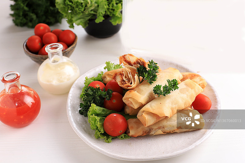 油炸春卷，流行的Lumpia或Popia。白色盘子，白色餐桌，配上辣酱和蛋黄酱。图片素材