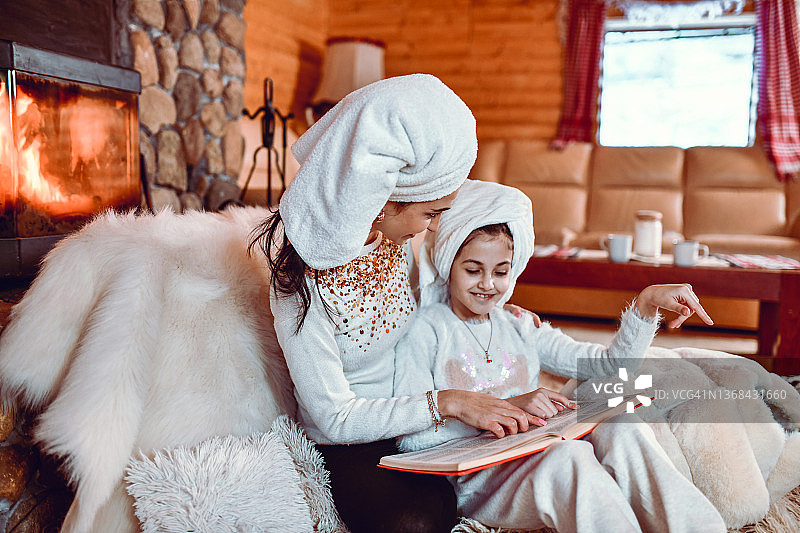 母亲和女儿沐浴后阅读山间小屋壁炉旁的故事图片素材