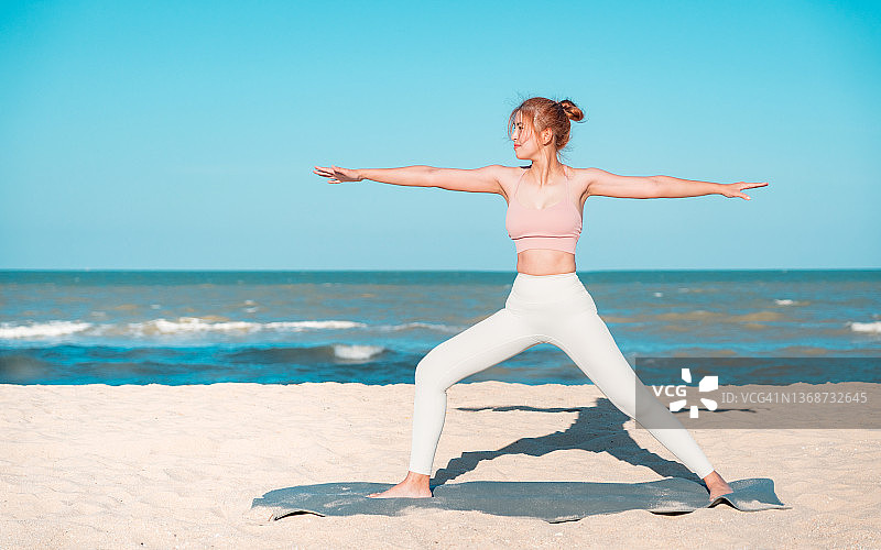 在海边练瑜伽的女人。年轻健康的瑜伽女子在日出时在海滩上练习瑜伽姿势。健康。放松的概念。图片素材