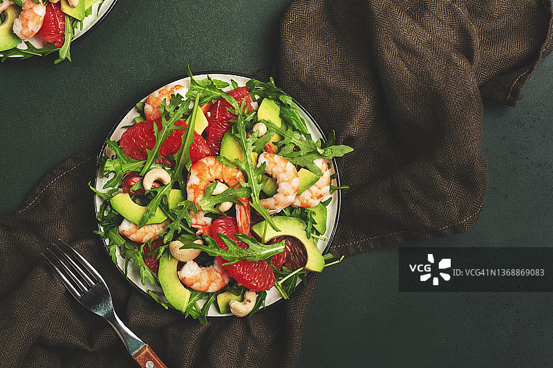虾仁，鳄梨，葡萄柚，芝麻菜和腰果的美味沙拉。低键深绿色表背景，俯视图，负空间图片素材