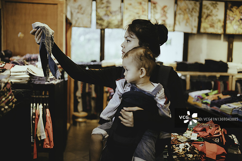 亚洲妇女在带着她的孩子展示店主的服装选择图片素材