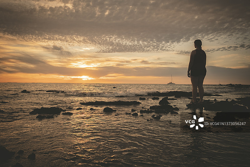 在夏威夷的海滩上，一个女人的剪影正看着引人注目的日落图片素材