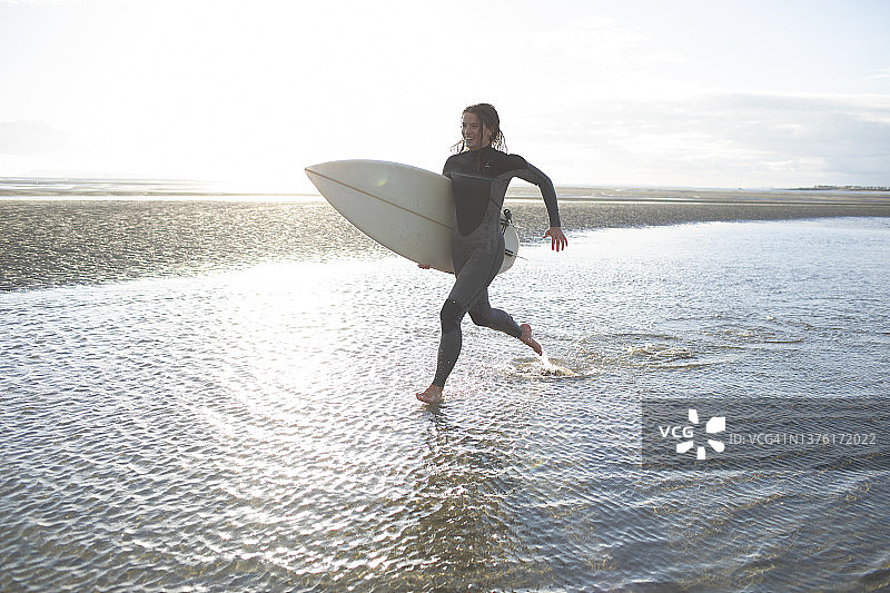 年轻的女性冲浪跑与冲浪板在阳光灿烂的海洋海滩冲浪图片素材