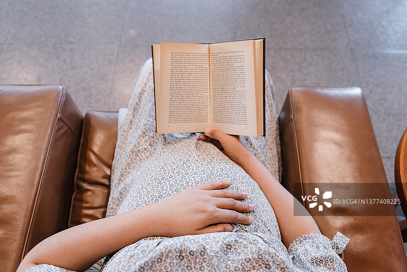 孕妇在客厅看书时摸肚子。图片素材
