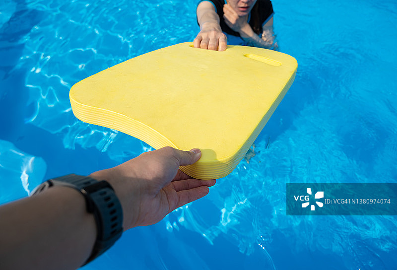 老师给想在游泳池练习游泳的女士一块黄色的游泳板。图片素材