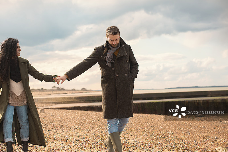 穿着冬衣的情侣手牵着手走在阳光明媚的海滩上图片素材