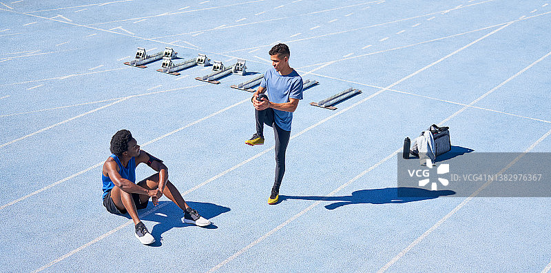 年轻的男性跑步者在阳光明媚的蓝色运动跑道上图片素材