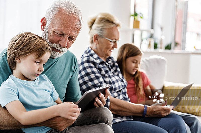 老年人和他们的小孙子在家里使用无线技术。图片素材