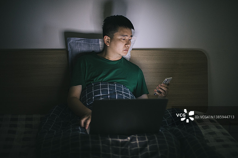 男人在床上使用电脑和智能手机图片素材