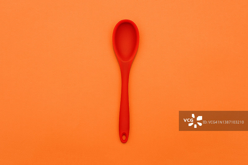 橙色背景上的红色硅胶勺。烹饪的背景。烹饪弗拉。美食博客。餐具。图片素材