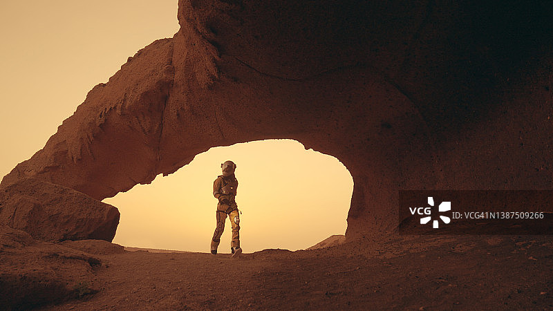 在火星上的孤独。女宇航员探索铁锈色的洞穴和岩石。触碰石头墙图片素材