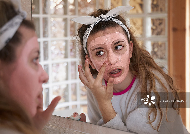 年轻的白人青少年使用面部护理霜反射在镜子上。医疗保健和医学概念。图片素材