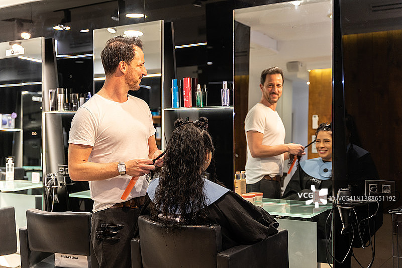 在豪华的现代美发沙龙，男发型师和湿卷发的女客户在做新发型图片素材