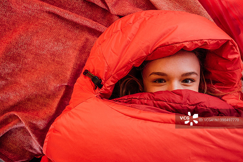 年轻女子从红色睡袋里往外看，毯子是红色的图片素材