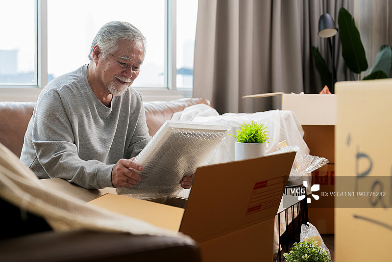 水平中景拍摄的成年老年亚洲人男性白胡子坐在地板上准备搬到新房子打包东西到箱子和胶带他们在客厅，搬家的想法概念图片素材