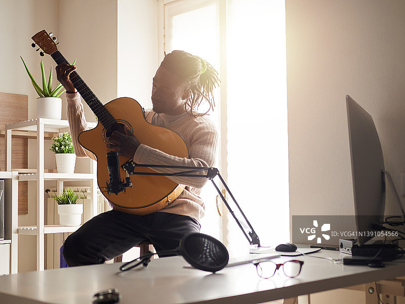 一个年轻人在家里一边唱歌一边弹吉他，一边录音图片素材