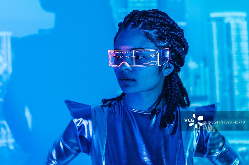 一个年轻的女人戴着蓝色背景的眼镜，穿着未来主义的银色套装。增强和虚拟现实概念，游戏，数字世界，未来技术，智能家居控制图片素材