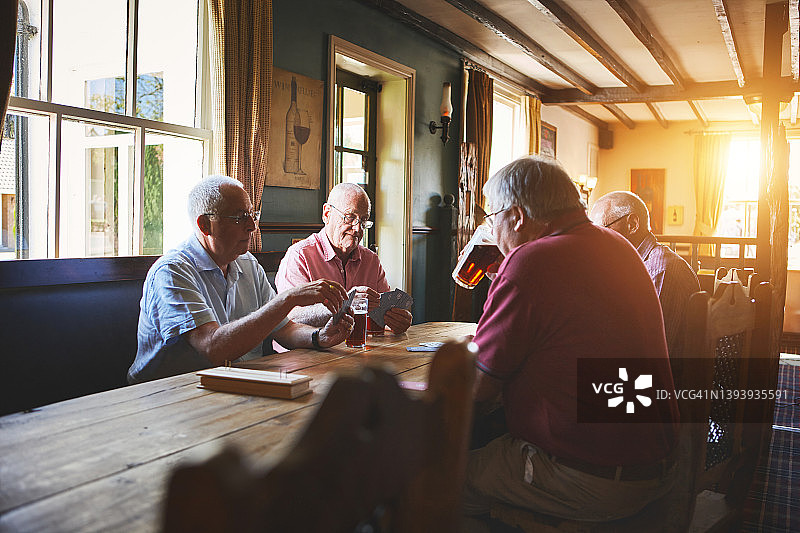 一群年长的男人坐在一起，在酒吧里打扑克，年长的朋友在酒吧里玩桥牌图片素材