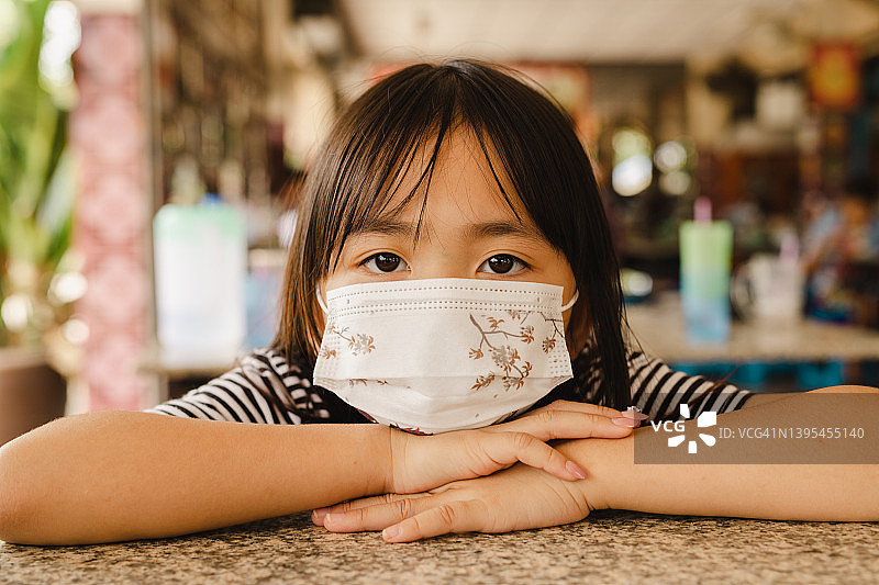 戴着外科口罩的泰国小女孩看着摄像机，以防感染冠状病毒或COVID-19。图片素材