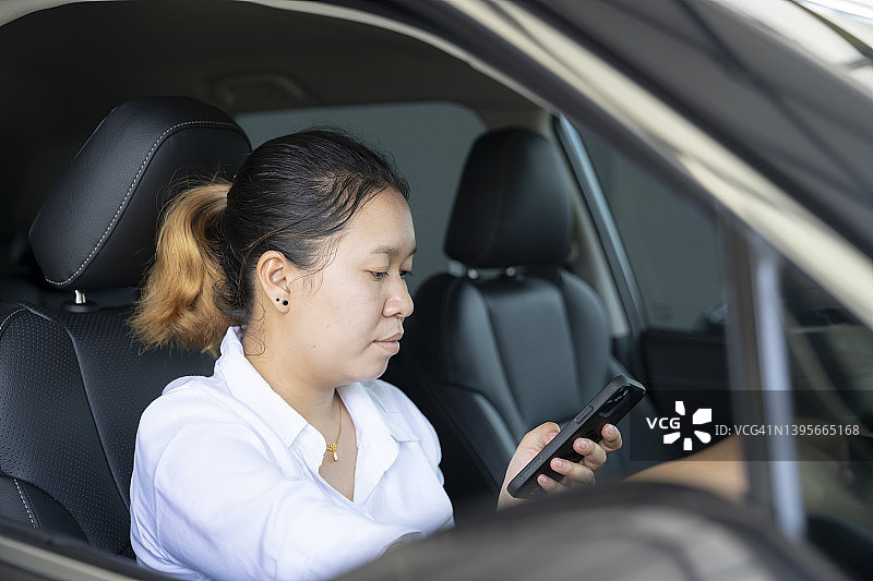 年轻的亚洲女性开车时使用手机图片素材