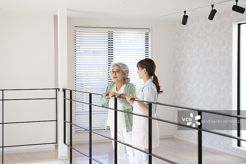 白天，一位老年妇女和一位年轻的亚洲护工在一家养老院的走廊里交谈。图片素材