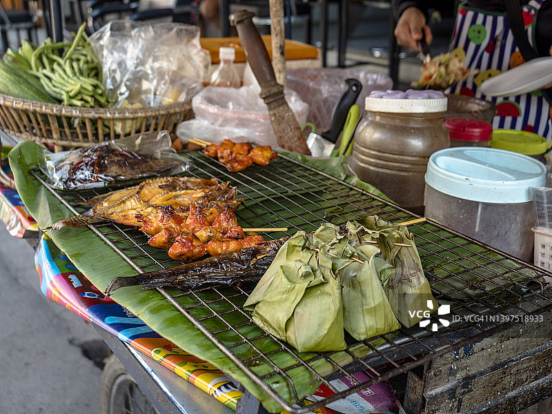 传统的亚洲泰国街烧烤食物正在准备在路上的摩托车食品卡车。各种五颜六色、辛辣的菜肴，既可以吃，也可以带走。对于上班族和下班回家的人来说，这是完美的小吃。分享泰国食物是一种传统。图片素材