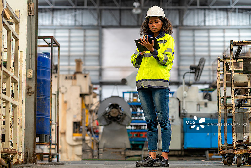 工程师使用平板电脑并在工厂工作。她正在重金属工业工厂检查工厂的设备。图片素材