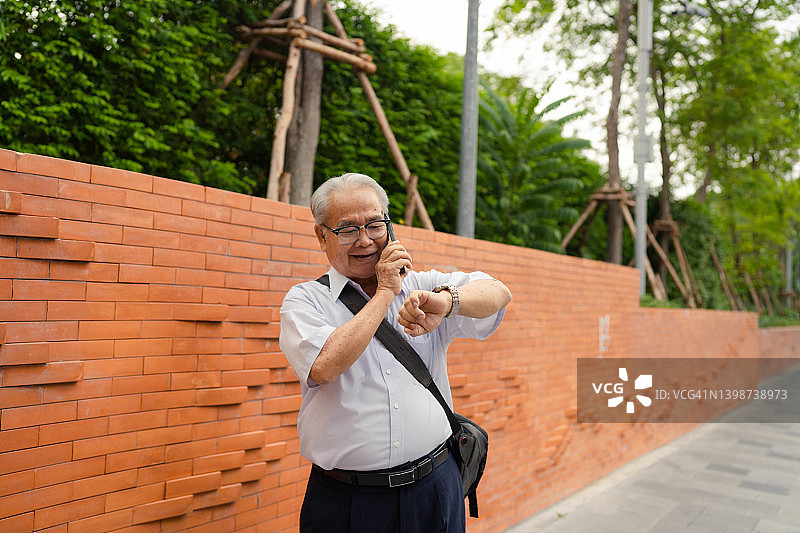 亚洲年长商人通过手机与客户交谈。图片素材