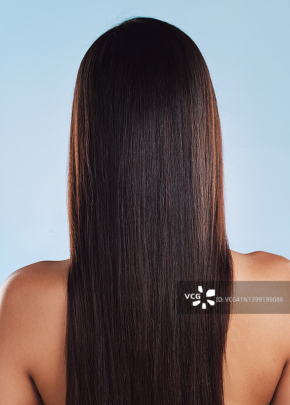 一个美丽的女人从后面，有着光滑、丝滑和健康的深褐色长发，在工作室的蓝色背景下摆姿势。模特经过美容院的染发和接发处理后的直发图片素材