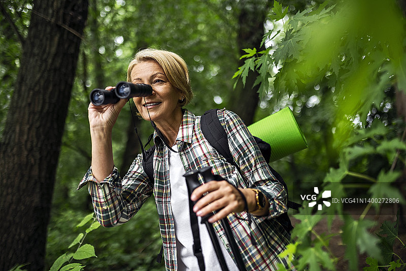 中年妇女在森林徒步旅行，探索通过望远镜看图片素材