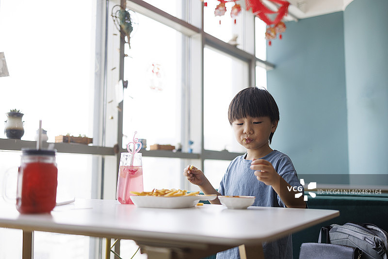 这个小男孩在餐厅里吃炸薯条图片素材