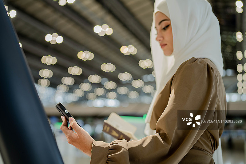 亚洲穆斯林妇女在机场使用登机机领取登机牌。图片素材